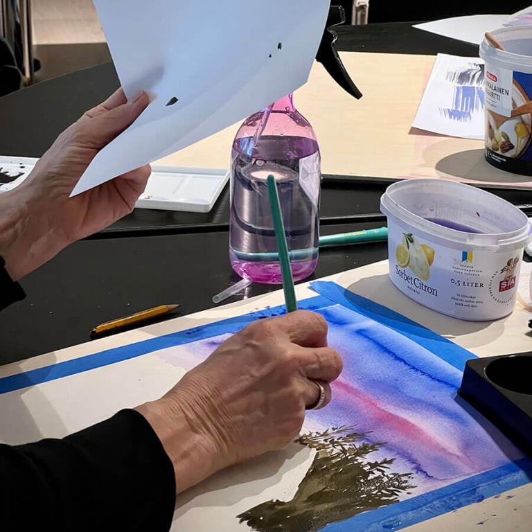 Bilden visar händer av en workshopdeltagare som målar.