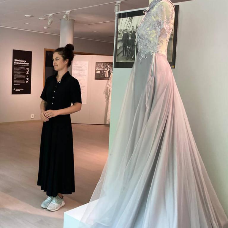 The artist Felicia Lindbäck next to one of the dresses in the exhibition