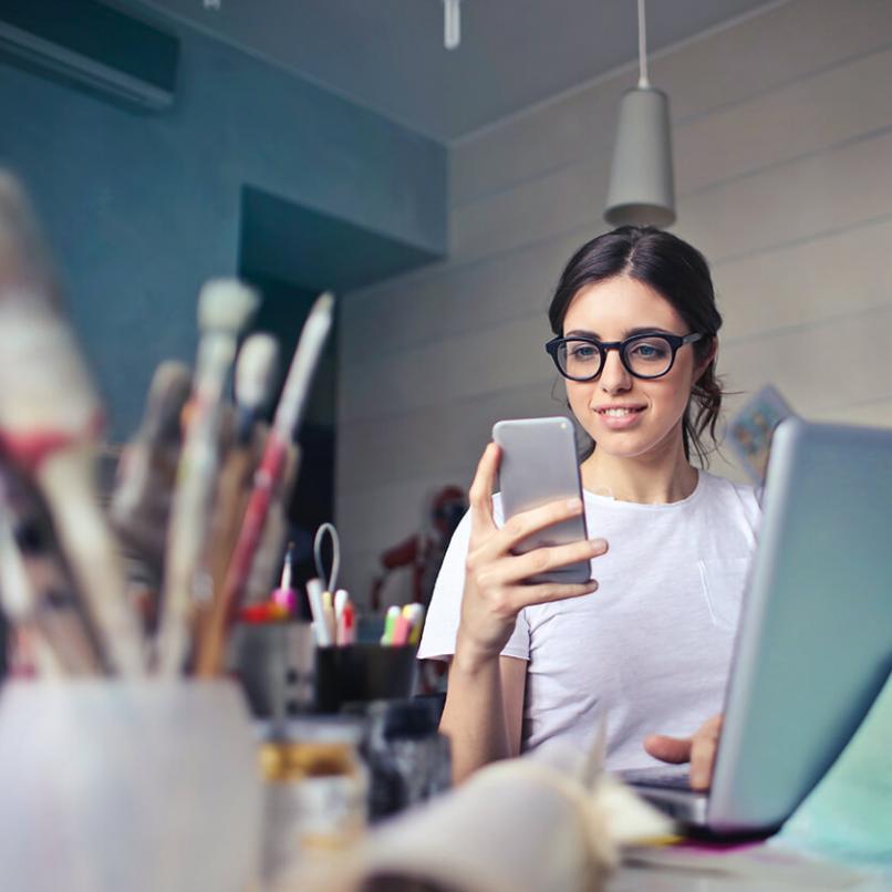 Picture of a woman sitting with phone and computer behind brushes and writing support application. Photo: Bruce Mars Unsplash